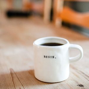 Kaffeetasse mit Beschriftung "Begin" auf Tisch