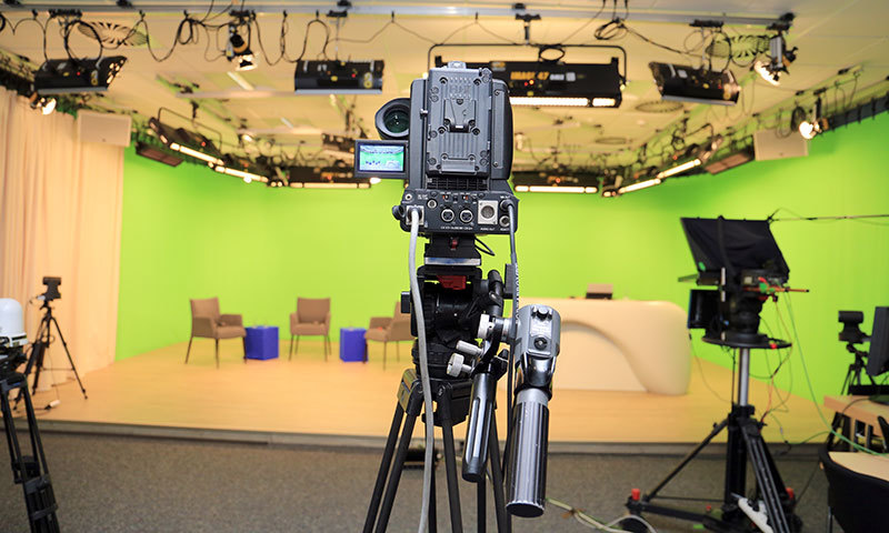 Foto des Videostudios mit Kamera im Vordergrund und Greenscreen-Bereich im Hintergrund