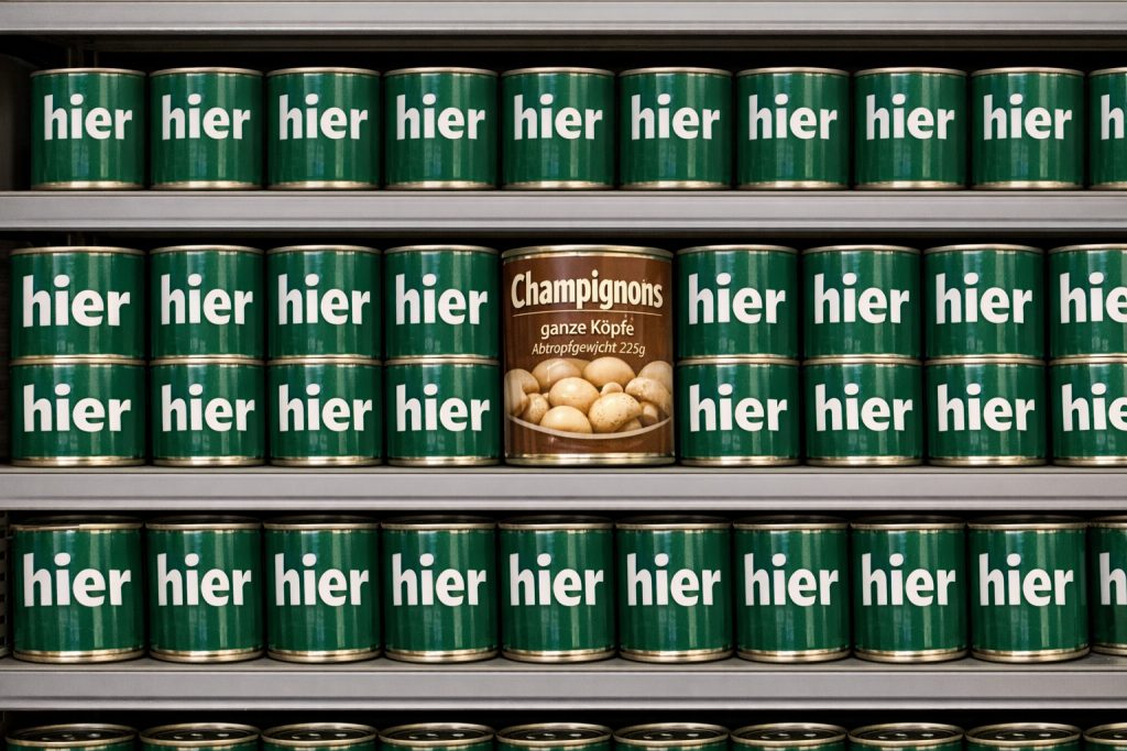 Mehrere Dosen mit der Aufschrift "hier" und eine Dose mit der Aufschrift "Champignons, ganze Köpfe, Abtropfgewicht 225g"