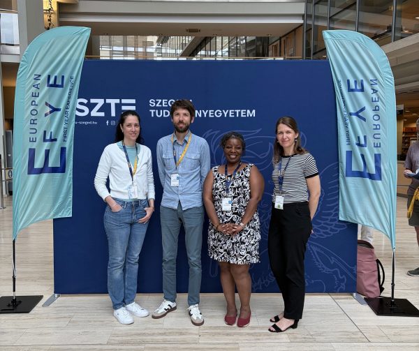 Foto von Réka Futász, Dr André Biedebeck, Dr Prue Goredema und Lídia Vinczéné Fekete vor einem Display der Tagung "European First Year Experience"
