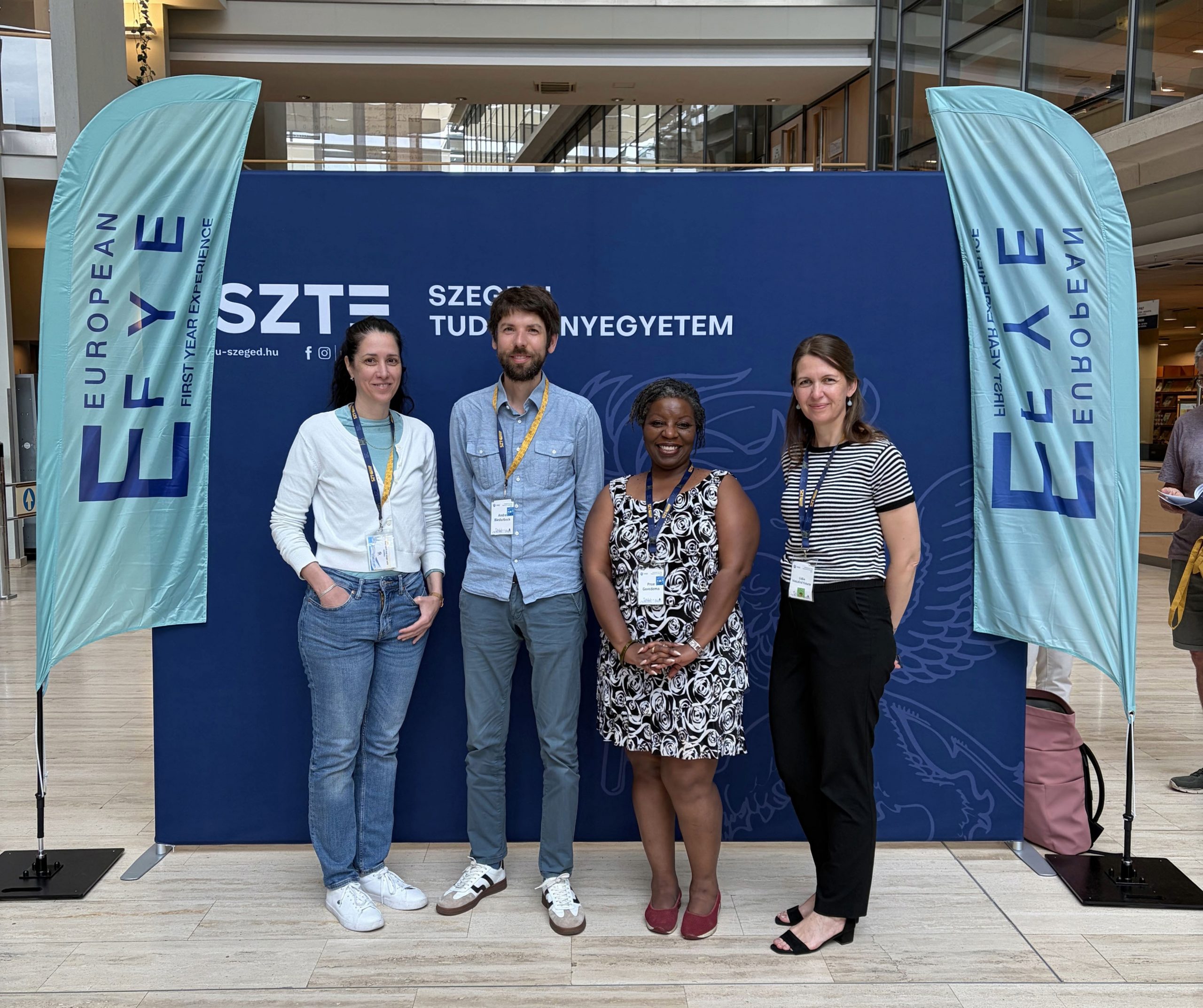 Foto von Réka Futász, Dr André Biedebeck, Dr Prue Goredema und Lídia Vinczéné Fekete vor einem Display der Tagung "European First Year Experience"